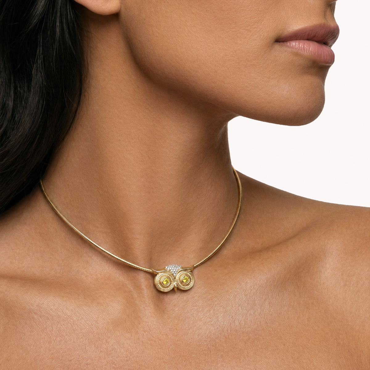 Close-up profile of a model wearing the SELIN KENT Athena necklace with yellow sapphire eyes on a gold omega chain against bare skin